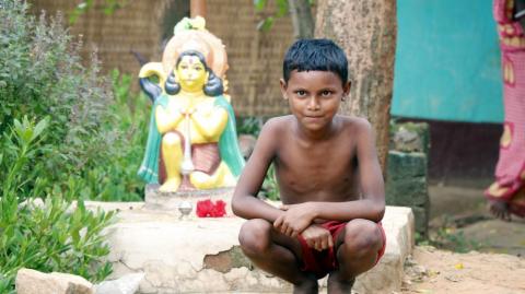 A smiling tribal boy in front of the idol of Lord Hanuman